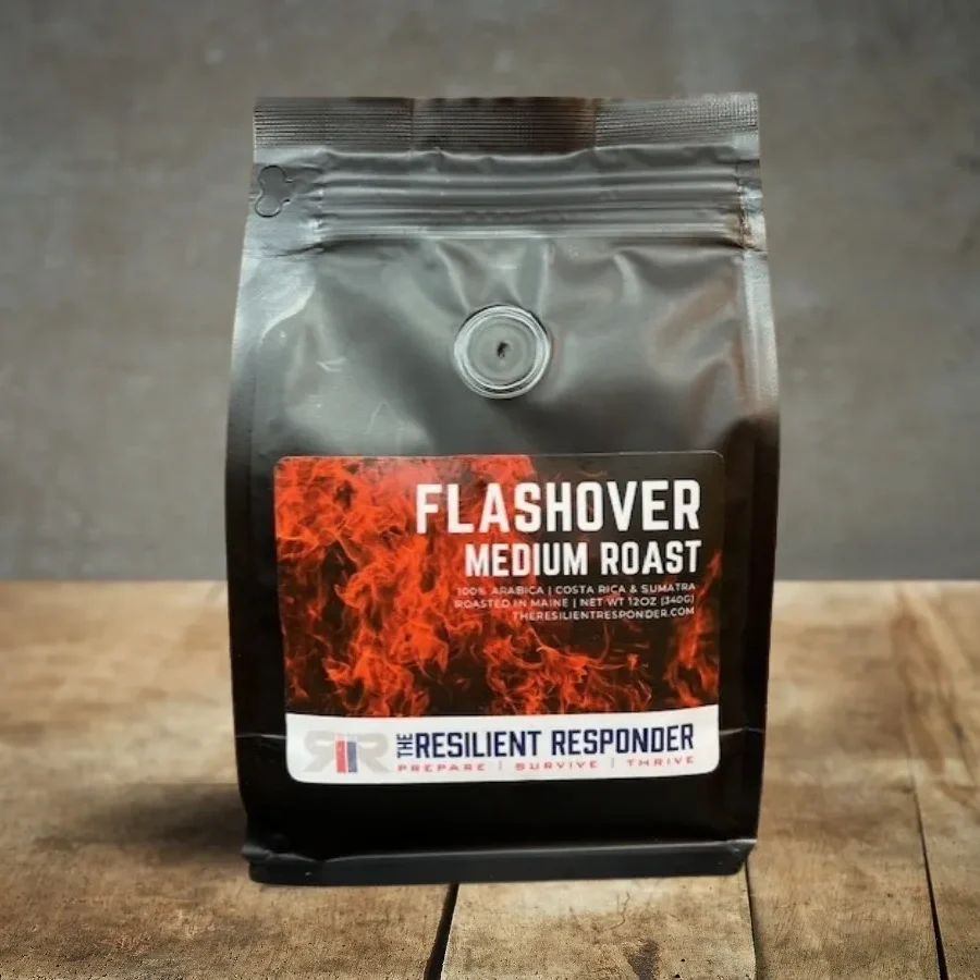 A bag of coffee labeled "Flashover Medium Roast" with a fire-themed design and "The Resilient Responder" logo at the bottom. The bag is on a wooden surface against a gray background.