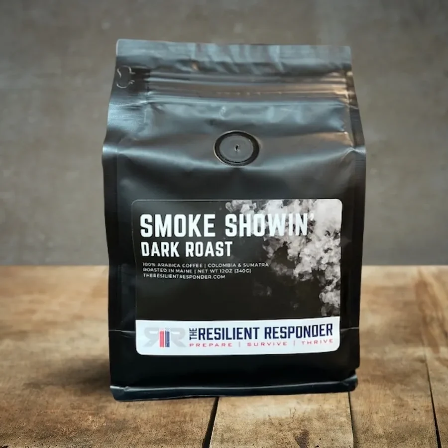 A black package of coffee labeled "Smoke Showin' Dark Roast" from The Resilient Responder, sitting on a wooden surface with a concrete wall in the background.