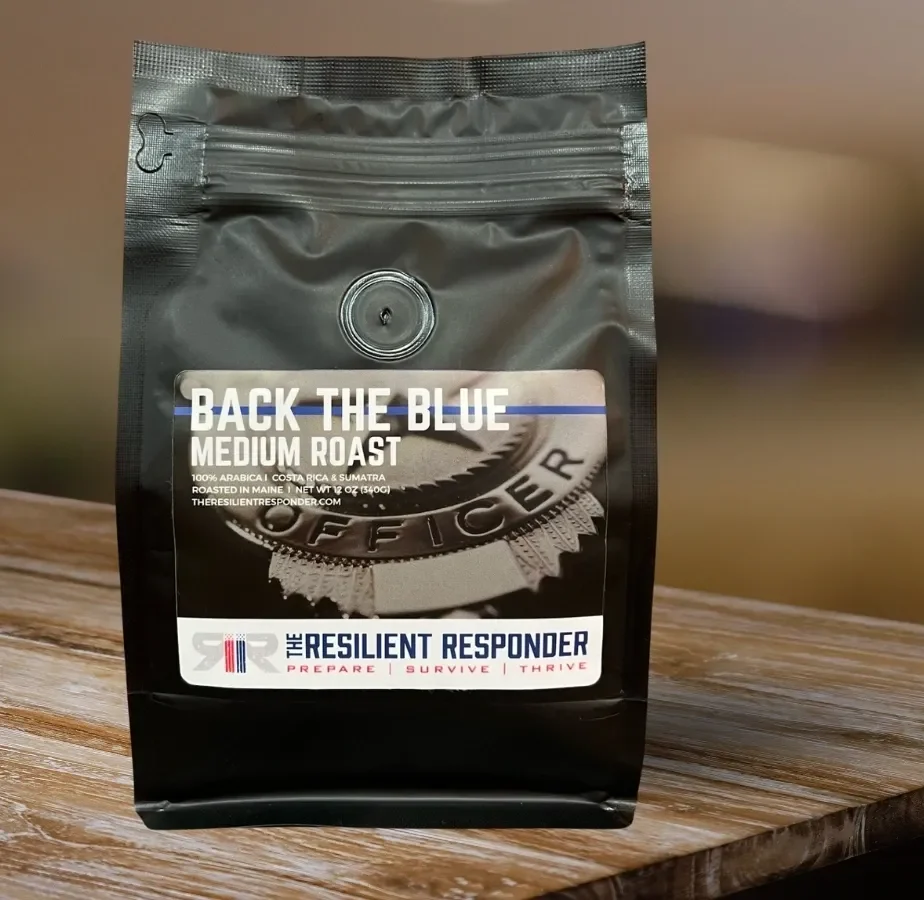 A black package labeled "Back the Blue Medium Roast" coffee rests on a wooden surface. The brand, "Resilient Responder," comes with the tagline "Prepare | Survive | Thrive.