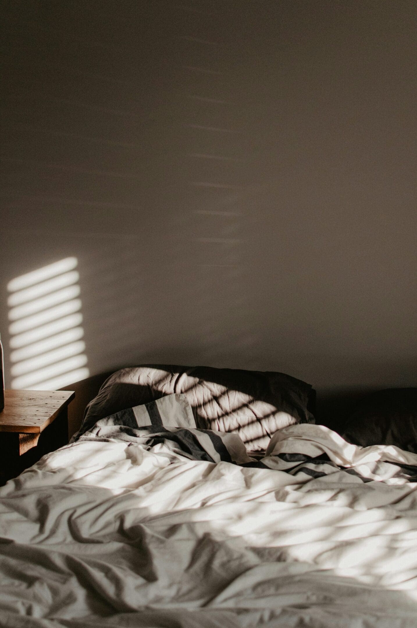 A bed with sheets folded up and the sun shining through.